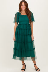 woman wearing a green tiered midi dress with short sleeves and a smocked bodice, styled with black strappy heels