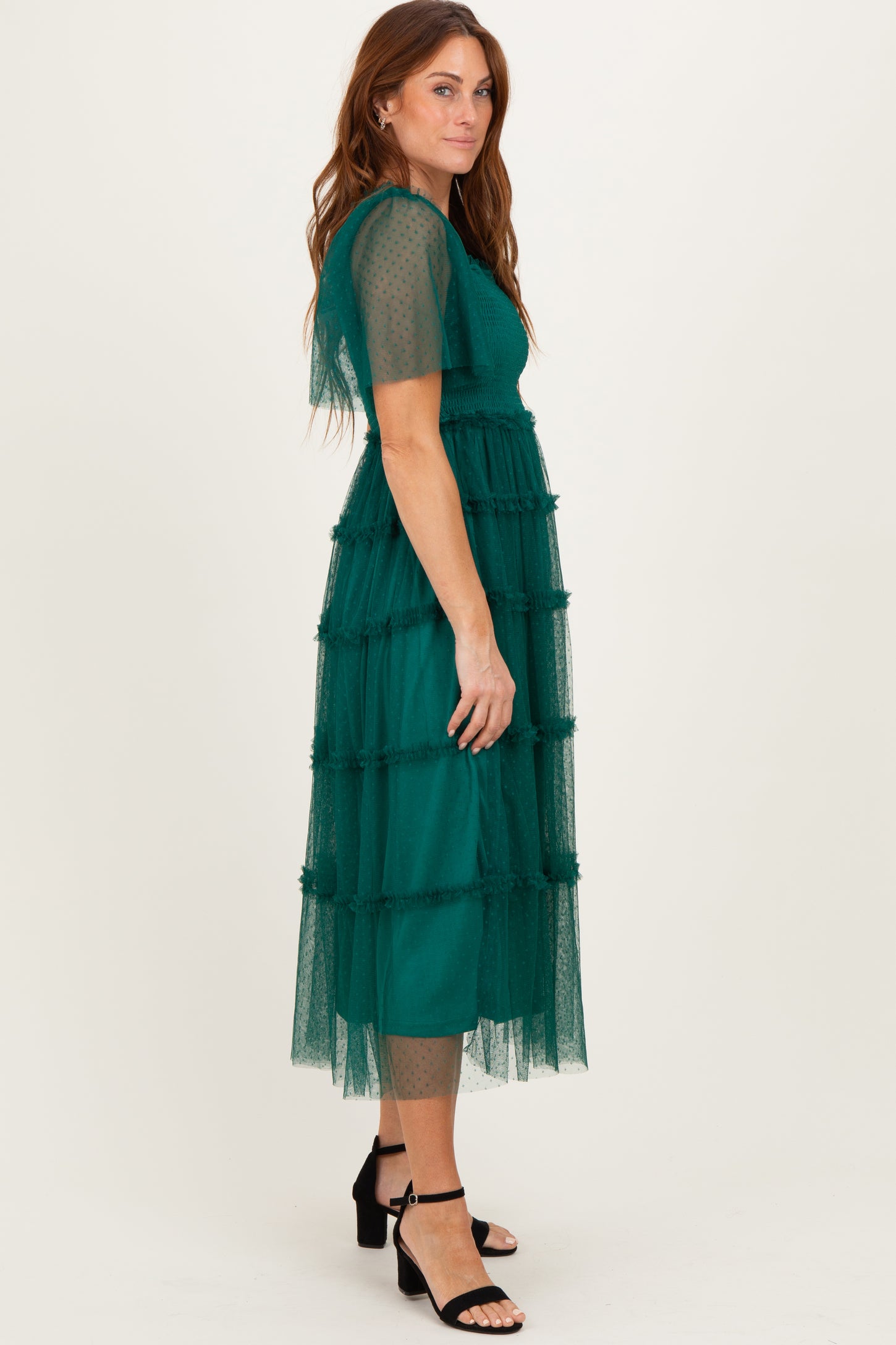 woman wearing a green tiered midi dress with tulle sleeves and a fitted bodice, styled with black heeled sandals