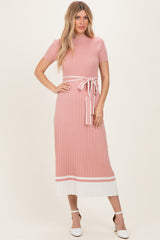 woman wearing a pink ribbed midi dress with a white tie waist and contrasting hem details, standing against a neutral background
