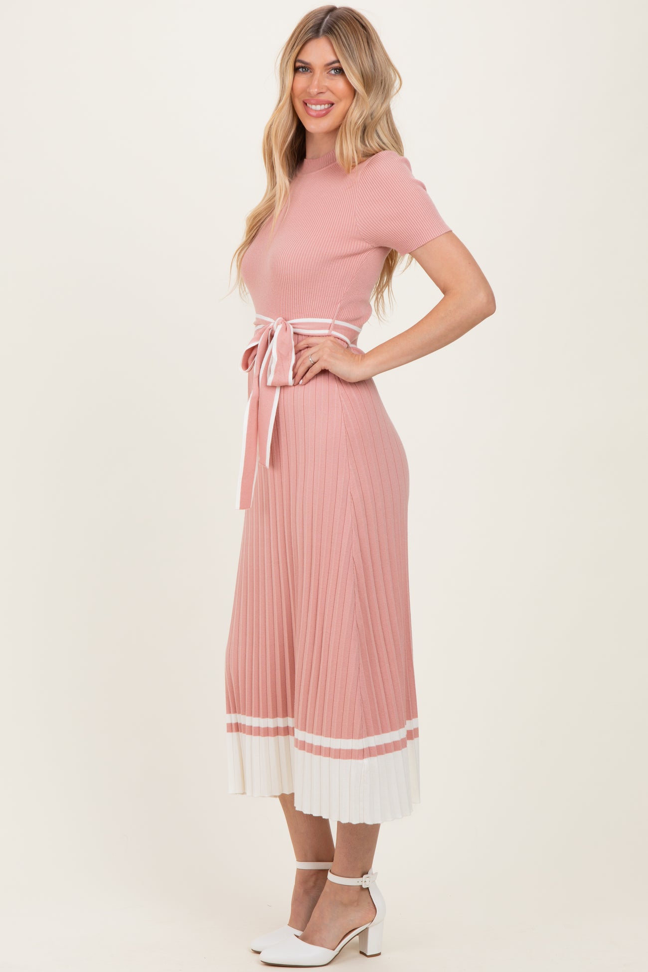 woman wearing a pink ribbed knit dress with short sleeves, a tie belt, and a pleated white hem