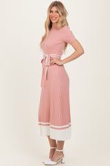 woman wearing a pink ribbed knit dress with short sleeves, a tie belt, and a pleated white hem