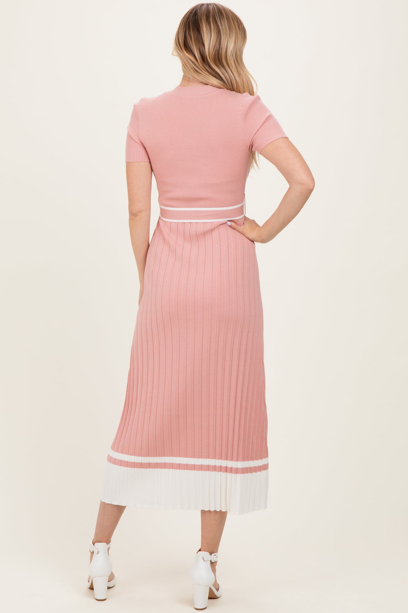 woman wearing a pink ribbed midi dress with short sleeves and white striped hem, shown from the back