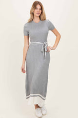 woman wearing a gray ribbed maxi dress with short sleeves and a tied waist, styled with white accents at the hem