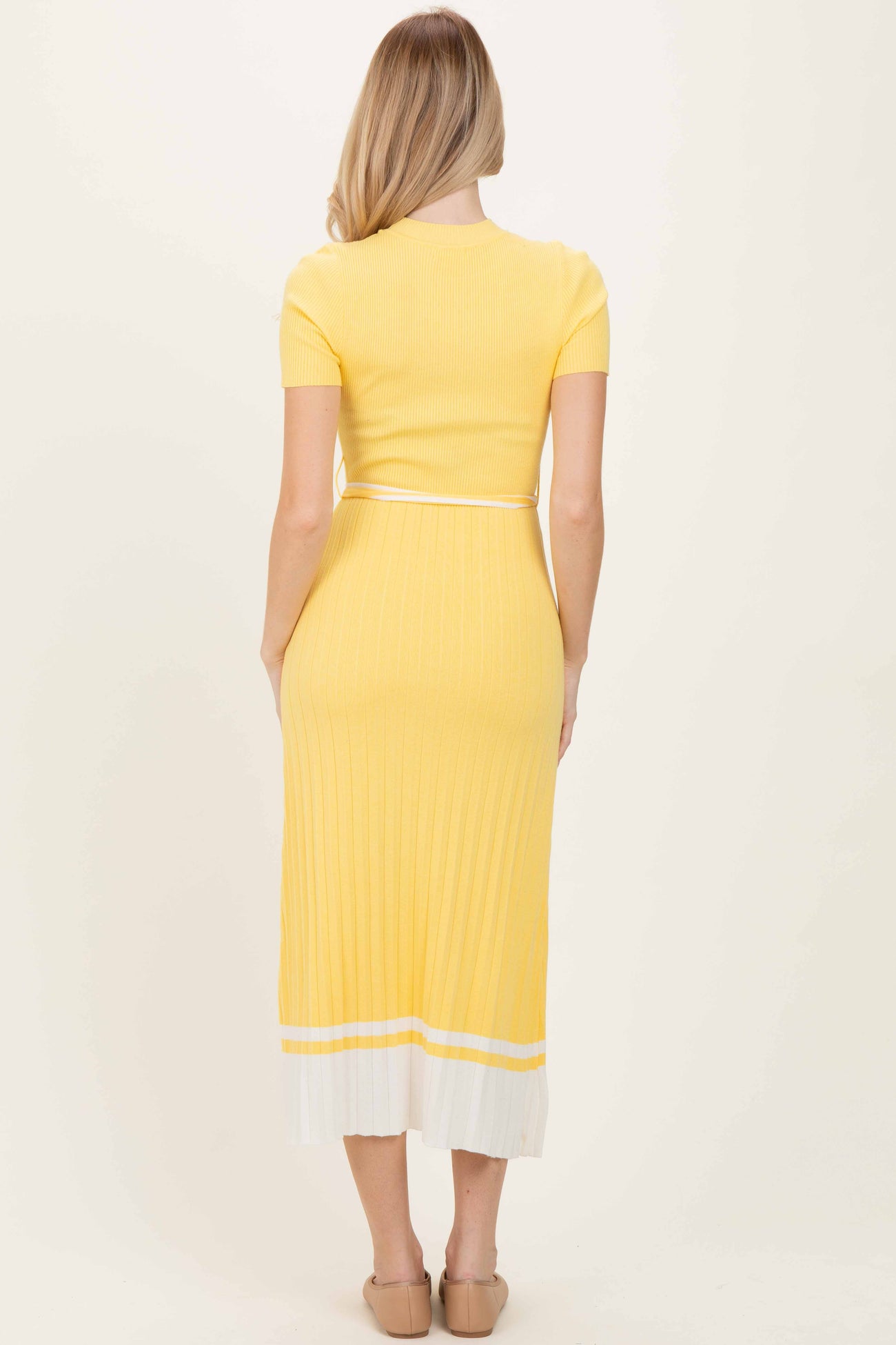 woman wearing a yellow ribbed midi dress with short sleeves and white stripe detail at the hem, showing the back view