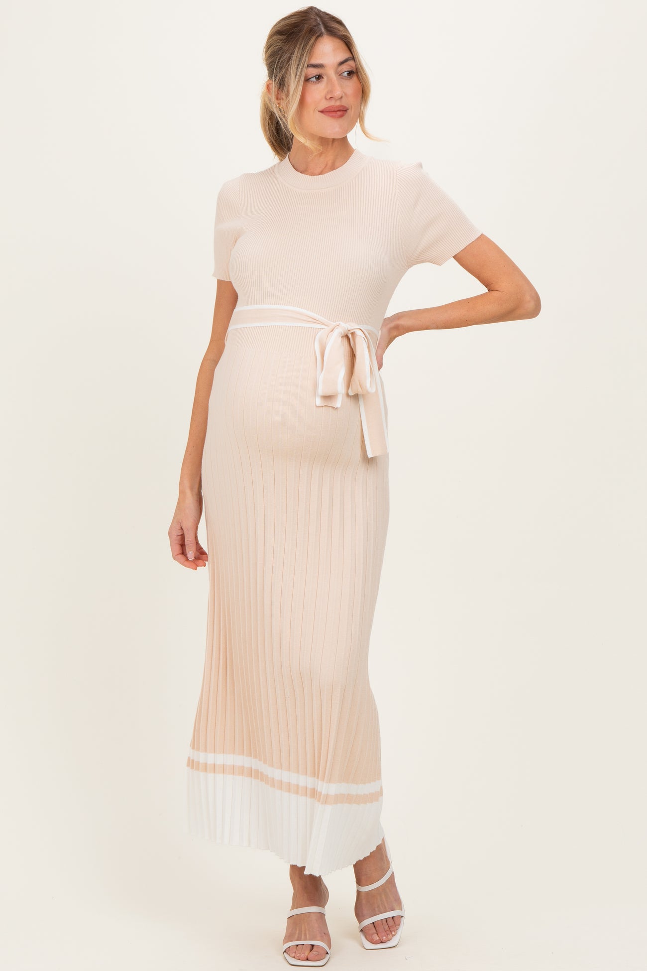 woman wearing a light pink ribbed maternity dress with a tie waist and a fitted silhouette, showing her baby bump