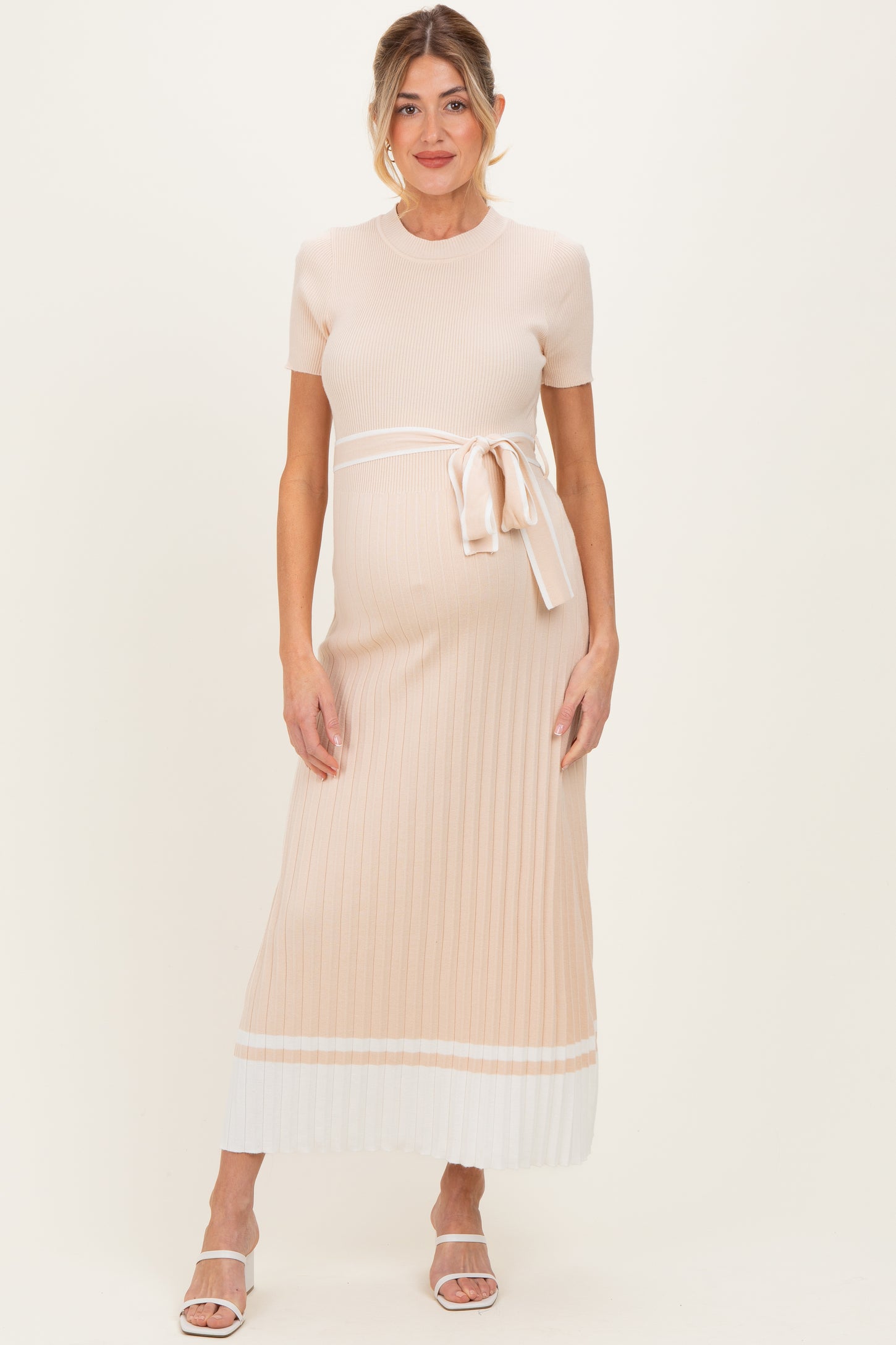 woman wearing a light pink ribbed maternity dress with a tie waist and white hem, featuring a visible baby bump
