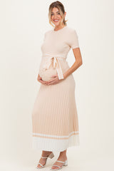 woman wearing a light pink ribbed maternity maxi dress with a white tie belt and holding her baby bump