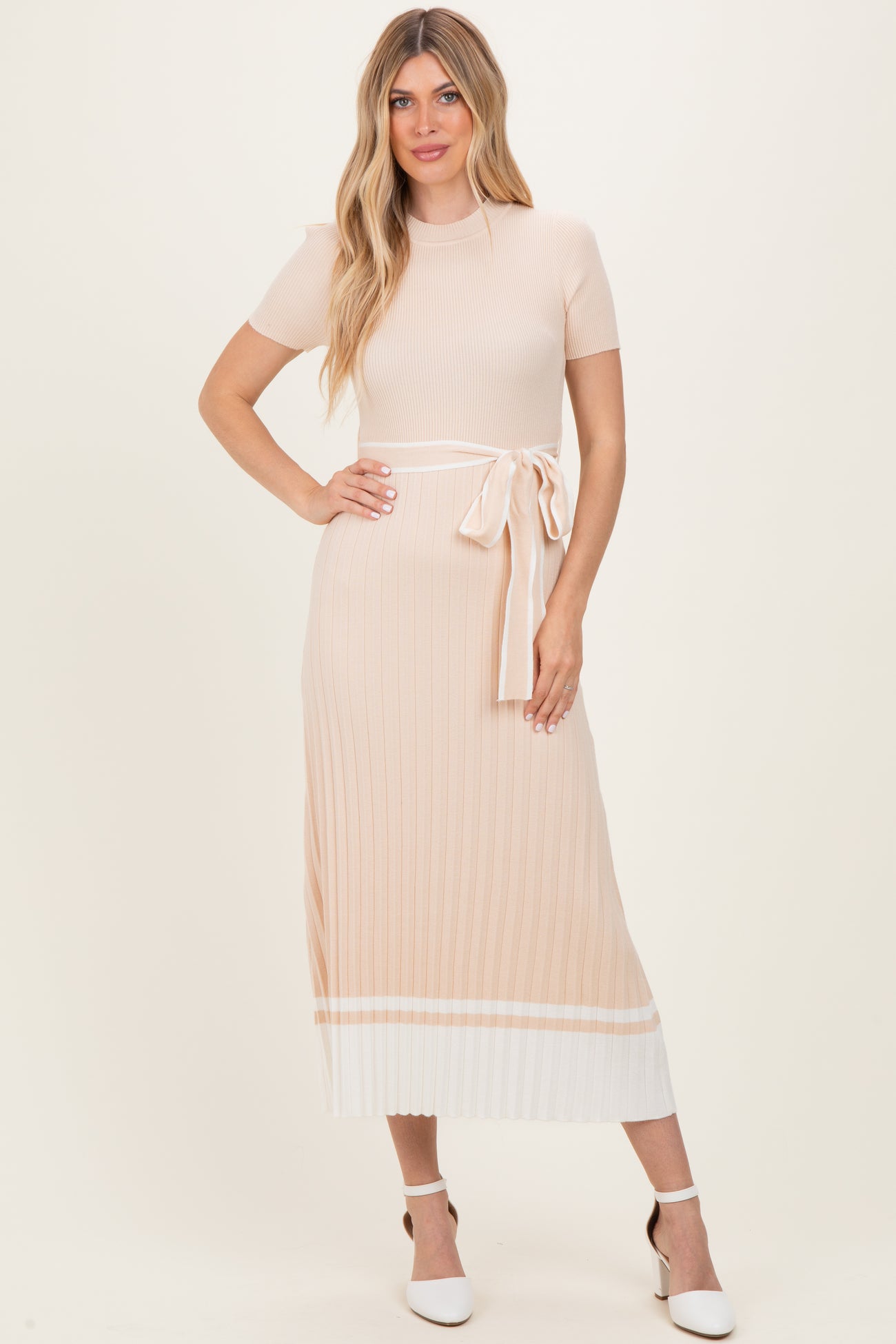 woman wearing a light peach ribbed midi dress with short sleeves and a tie belt detail, paired with white heels