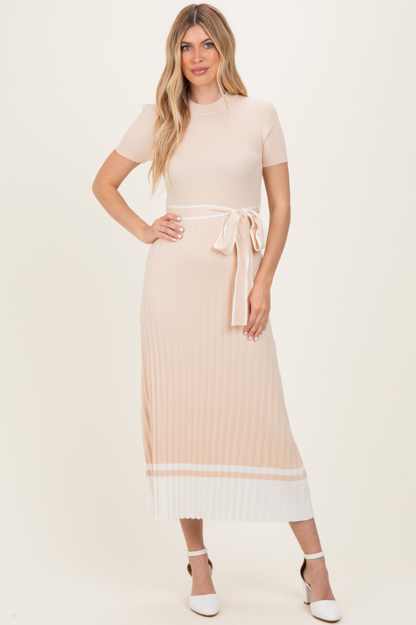 woman wearing a light peach ribbed midi dress with short sleeves and a tie belt detail, paired with white heels