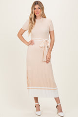 woman wearing a light peach ribbed midi dress with short sleeves and a tie belt detail, paired with white heels