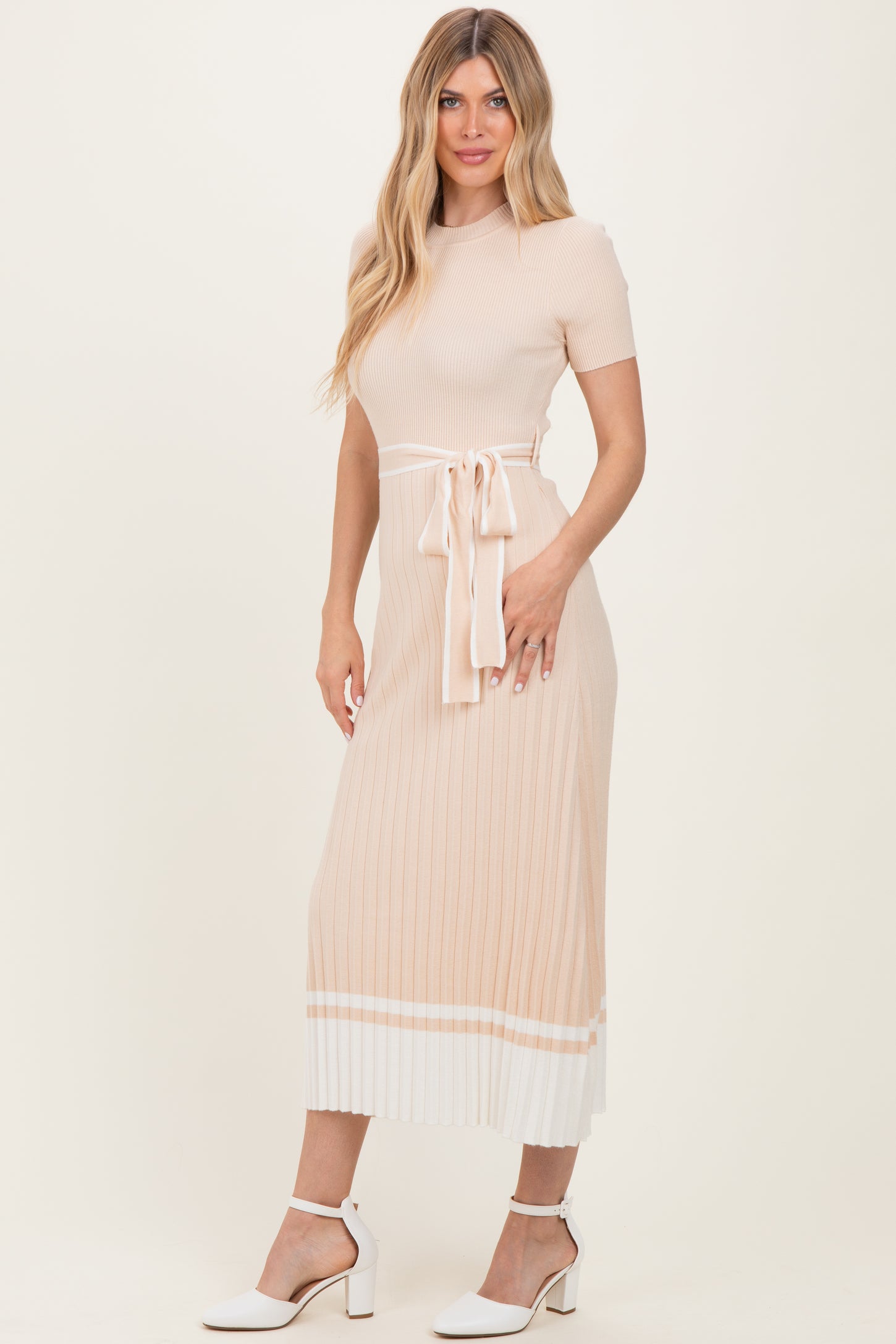 woman wearing a ribbed beige midi dress with a tie waist detail and white stripe accents on the hem