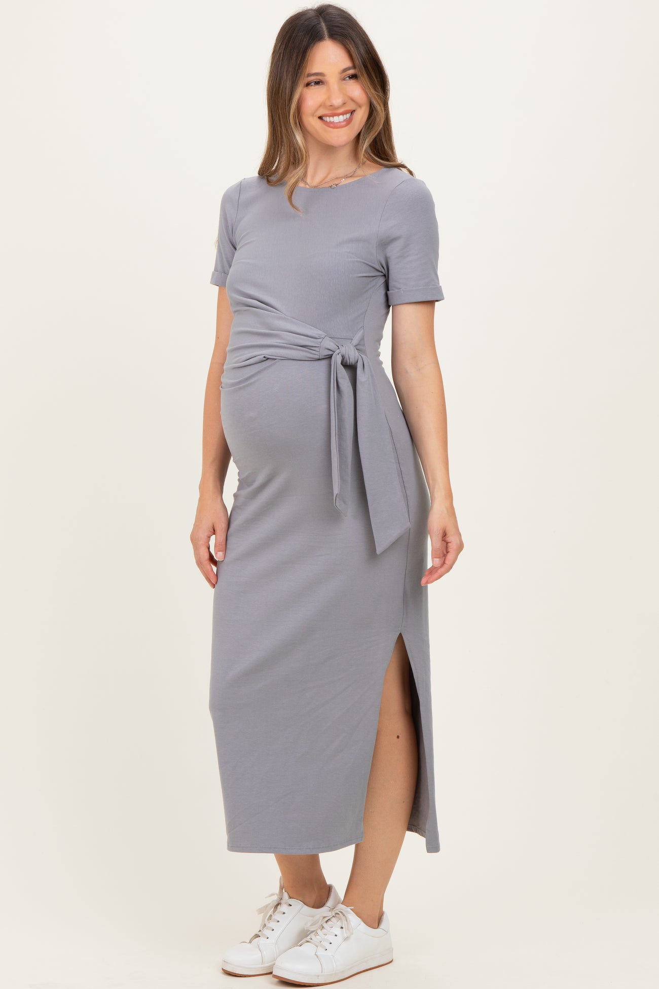 woman wearing a gray maternity maxi dress with a tie waist and side slit, showing off her baby bump