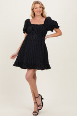 woman wearing a black maternity dress with puff sleeves and ruffled hem, styled with strappy black heels