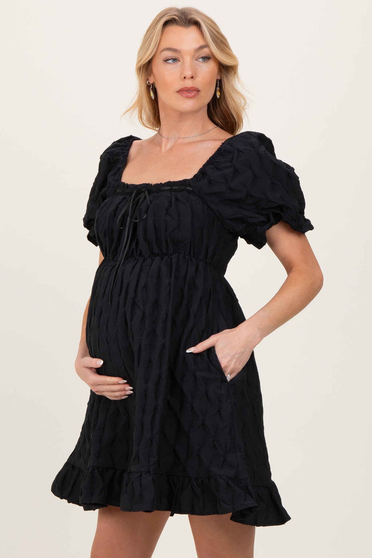 woman wearing a black puff sleeve maternity dress with a cinched waist and pockets, showing her baby bump