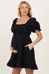 woman wearing a black puff sleeve maternity dress with a cinched waist and pockets, showing her baby bump