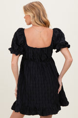 woman wearing a black maternity dress with puff sleeves and a ruffled hem, showing the back view