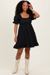 woman wearing a black short puff sleeve dress with ruffles and a square neckline, smiling and posing with one hand on her hip