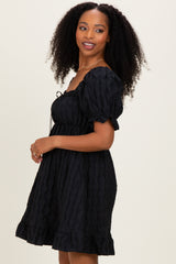 woman wearing a black short puff sleeve dress with a tie front and ruffled hemline