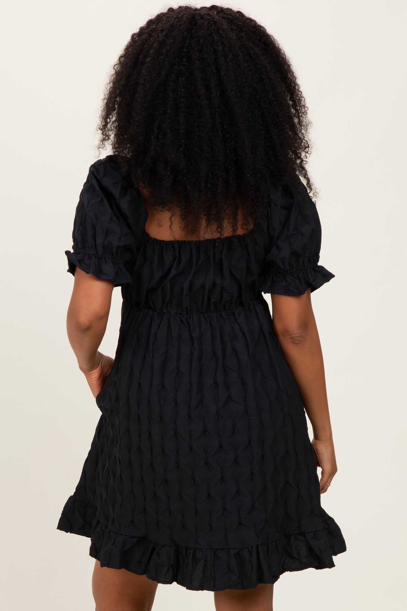 woman wearing a black short puff sleeve dress with a ruffled hem and textured fabric from the back