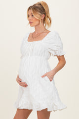 woman wearing a white short puff sleeve maternity dress with a square neckline and pockets, holding her baby bump