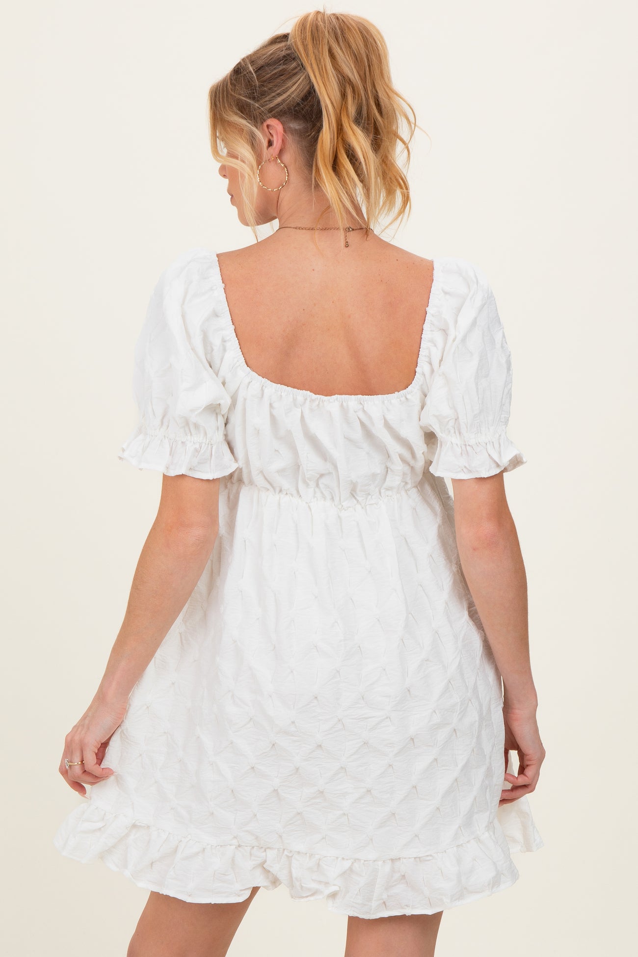 woman wearing a white short sleeve maternity dress with a ruched waist and ruffled hemline, showing a baby bump