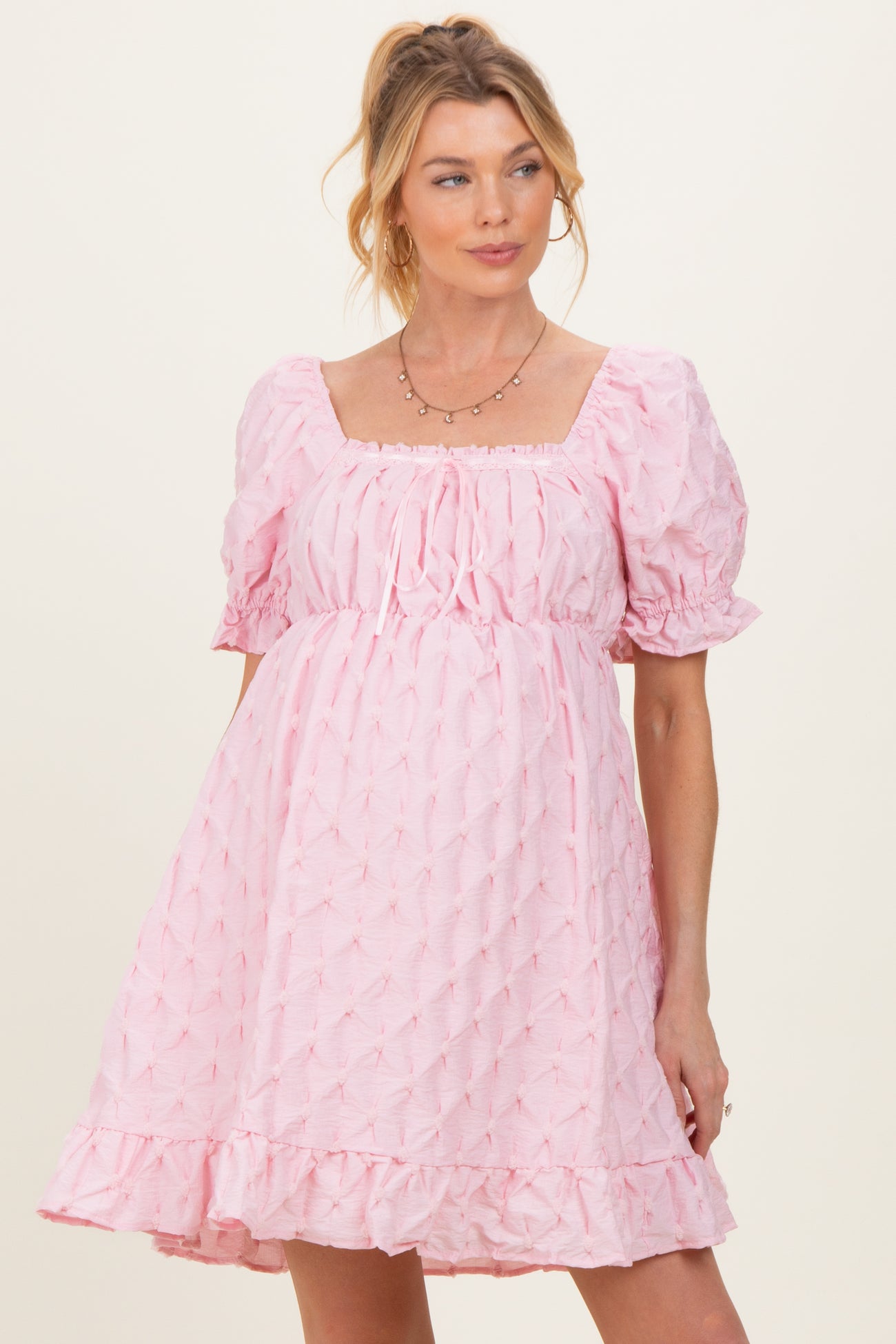 woman wearing a pink puff sleeve maternity dress with a square neckline and ruffled hem, showcasing her baby bump