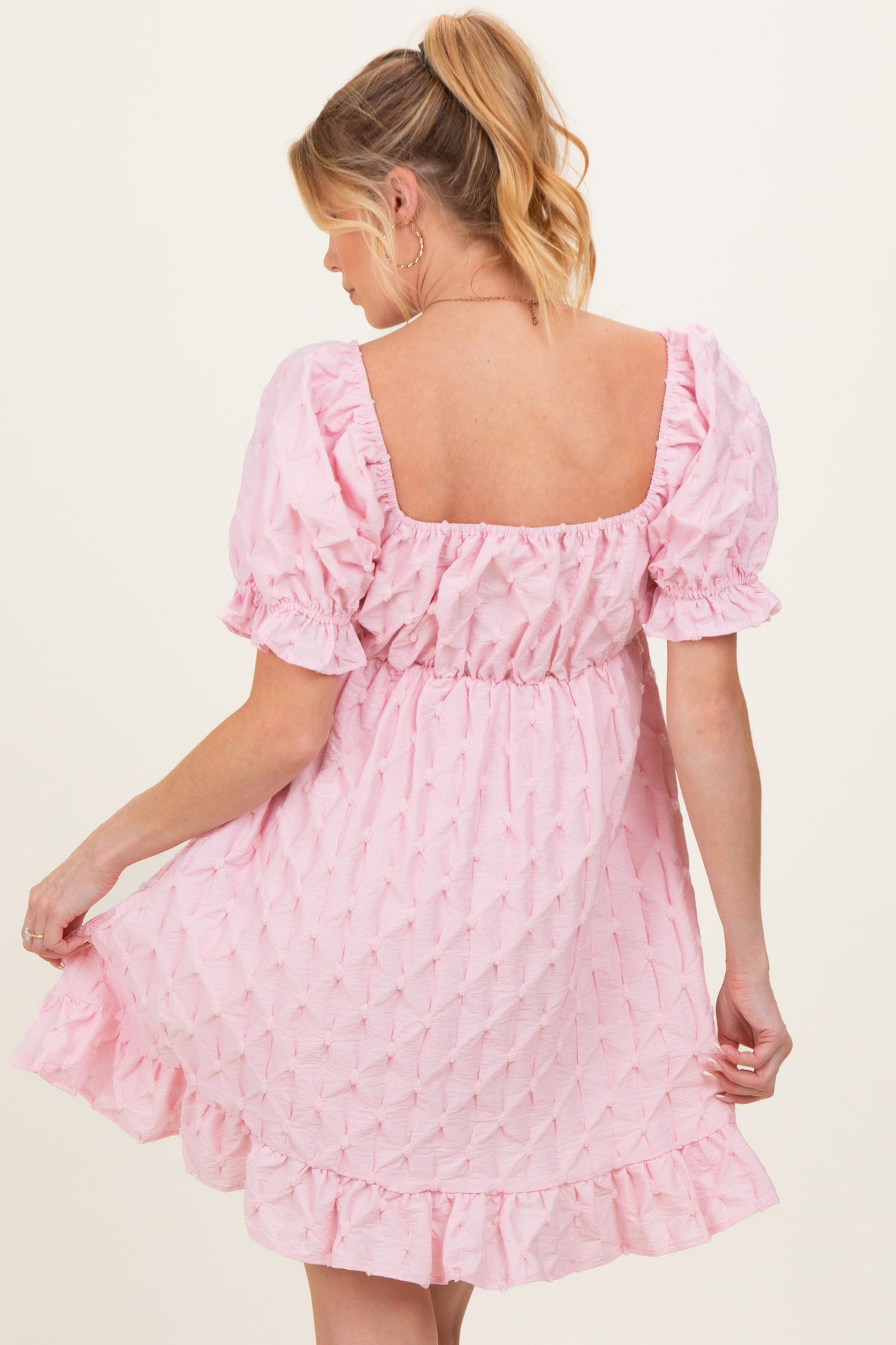 woman wearing a light pink maternity dress with puff sleeves and a ruffled hem, showing her back
