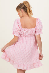 woman wearing a light pink maternity dress with puff sleeves and a ruffled hem, showing her back