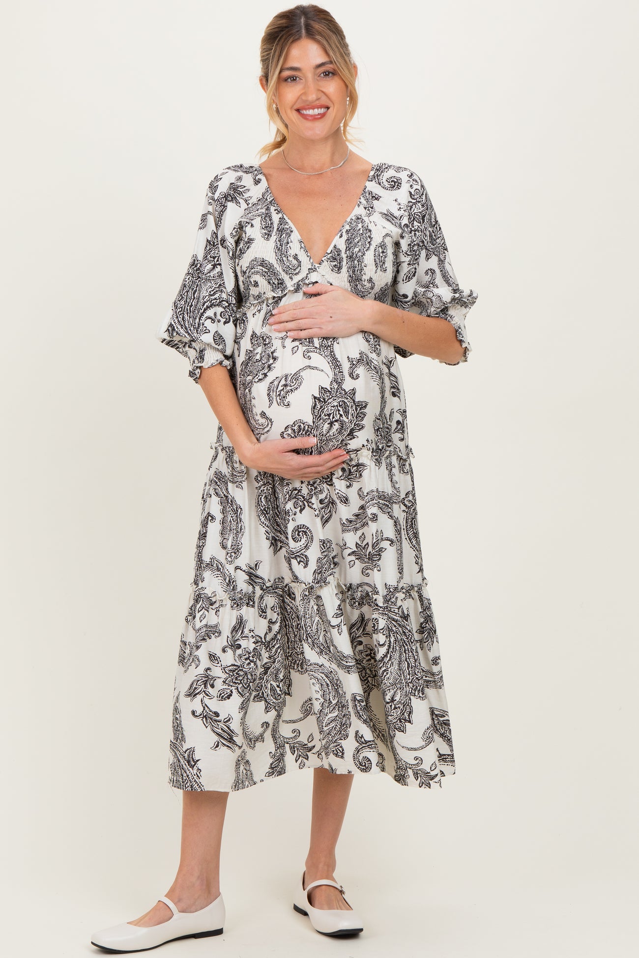 woman wearing a black and white paisley print maternity dress and cradling her baby bump