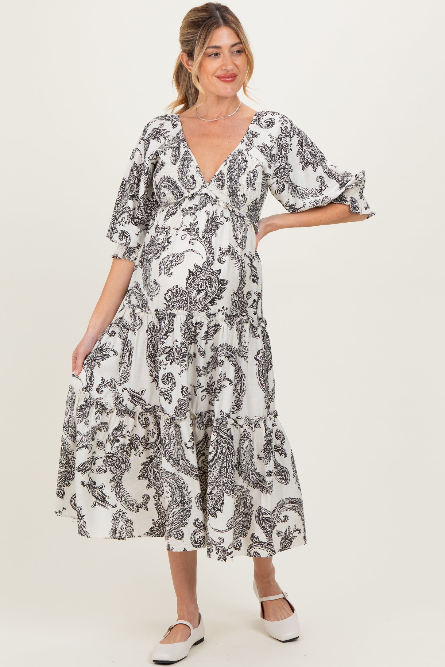 woman wearing a black and white printed maternity dress with a v-neck and tiered skirt, holding her baby bump