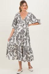 woman wearing a black and white printed maternity dress with a v-neck and tiered skirt, holding her baby bump