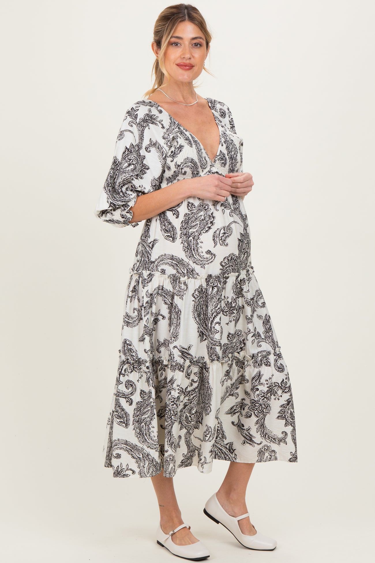 woman wearing a black and white paisley print maternity dress with a deep v-neck and balloon sleeves, showcasing her baby bump