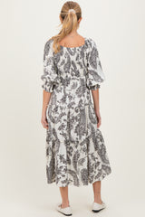 woman wearing a black and white paisley print maternity dress with a tiered skirt and puff sleeves, showing her baby bump