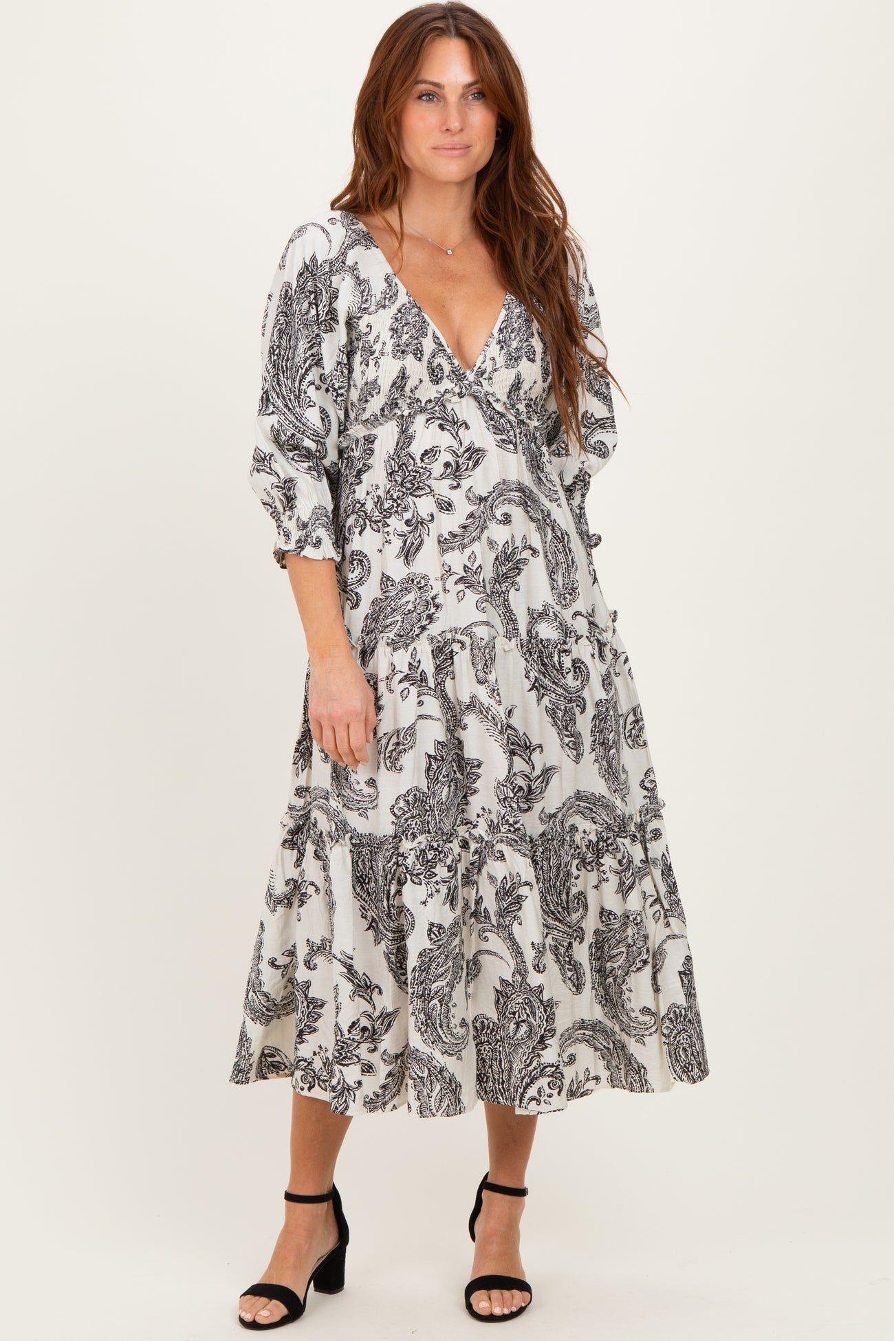 woman wearing a black and white patterned long sleeve midi dress with a v-neckline and tiered skirt.