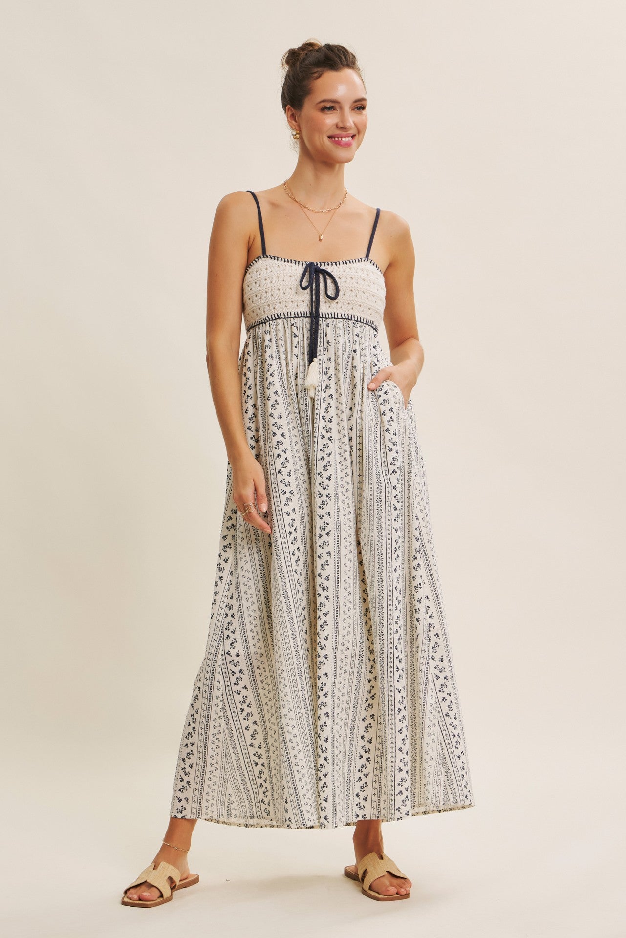 woman wearing a white maxi dress with navy patterns, adjustable spaghetti straps, and side pockets