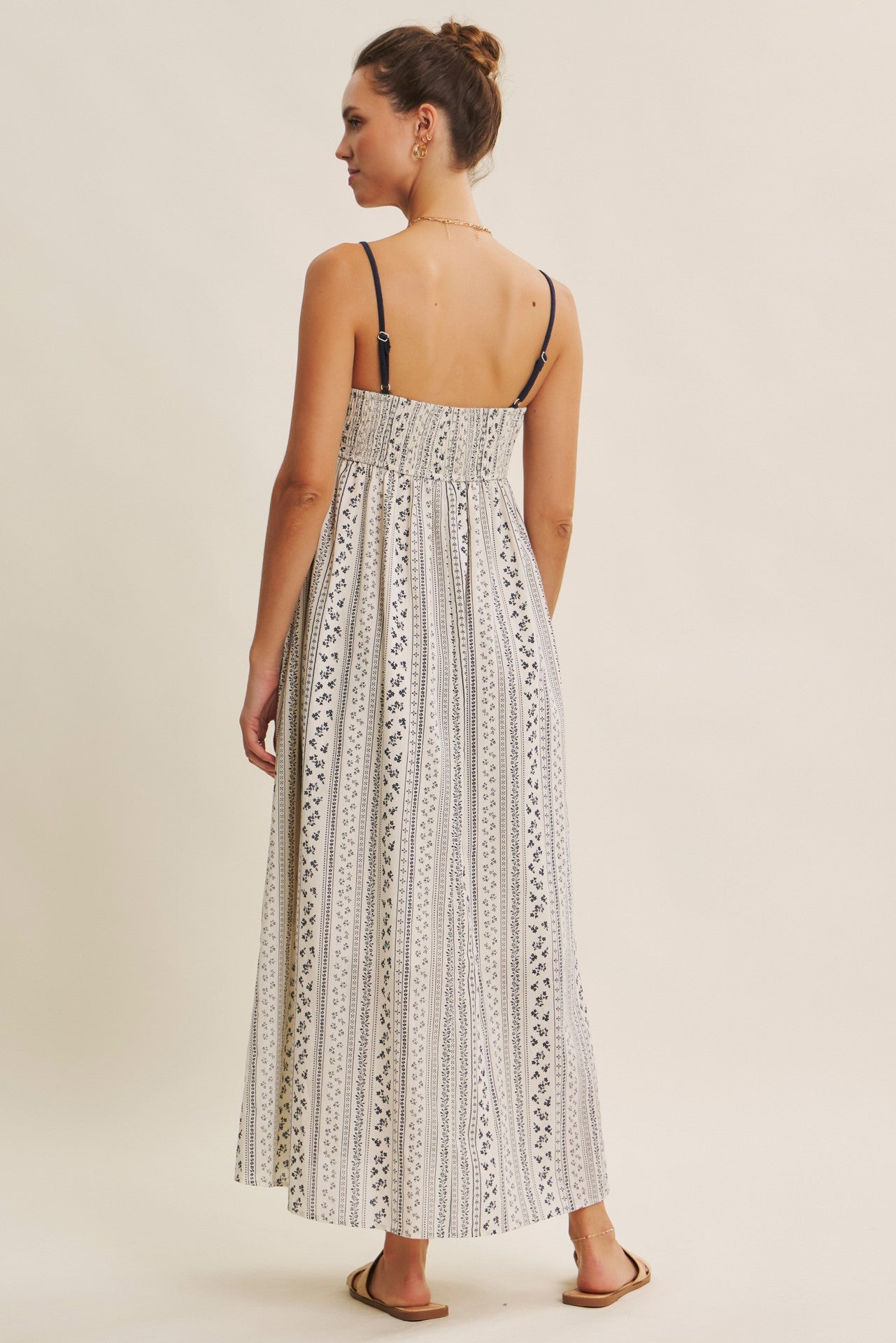 woman wearing a back view of a long white and navy patterned maxi dress with thin straps
