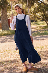 woman wearing a navy blue tiered maxi dress with button details and a white long sleeve top, standing on a swing