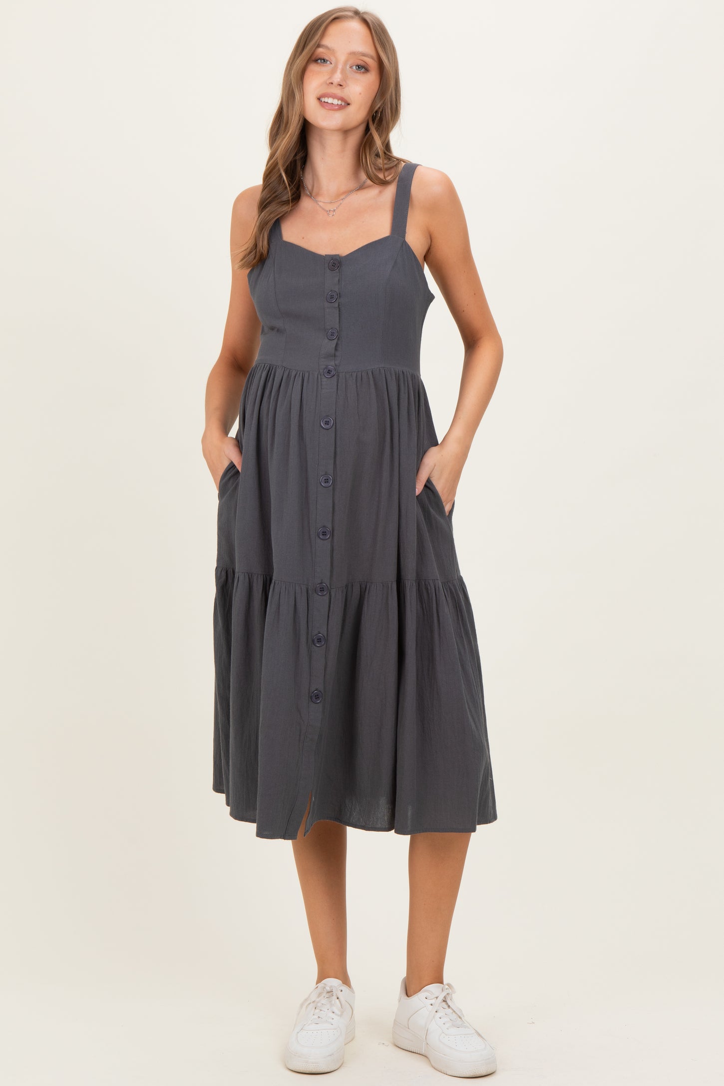 woman wearing a dark gray maternity midi dress with button details and pockets, displaying her baby bump