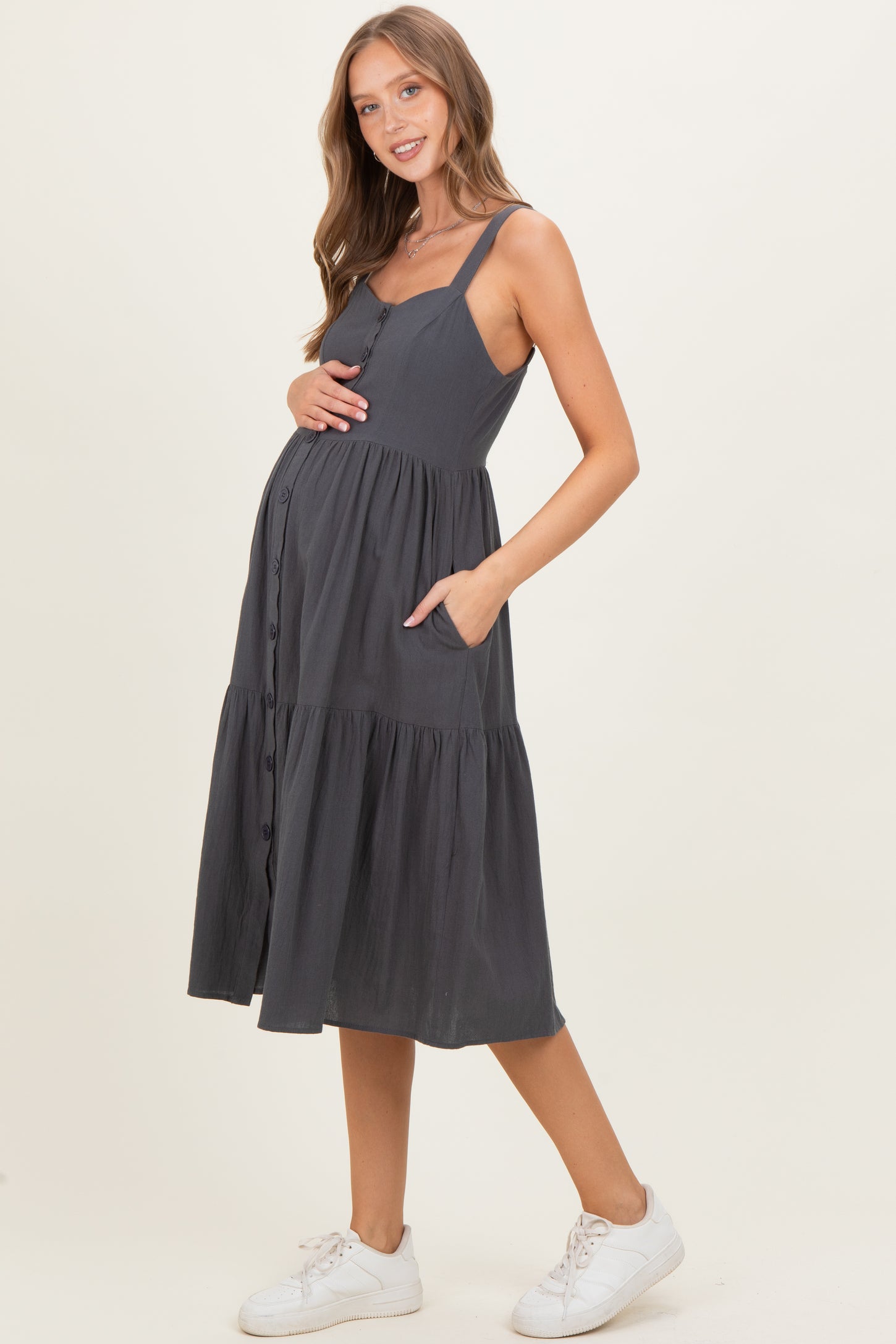 woman wearing a gray maternity midi dress with buttons and pockets, holding her baby bump