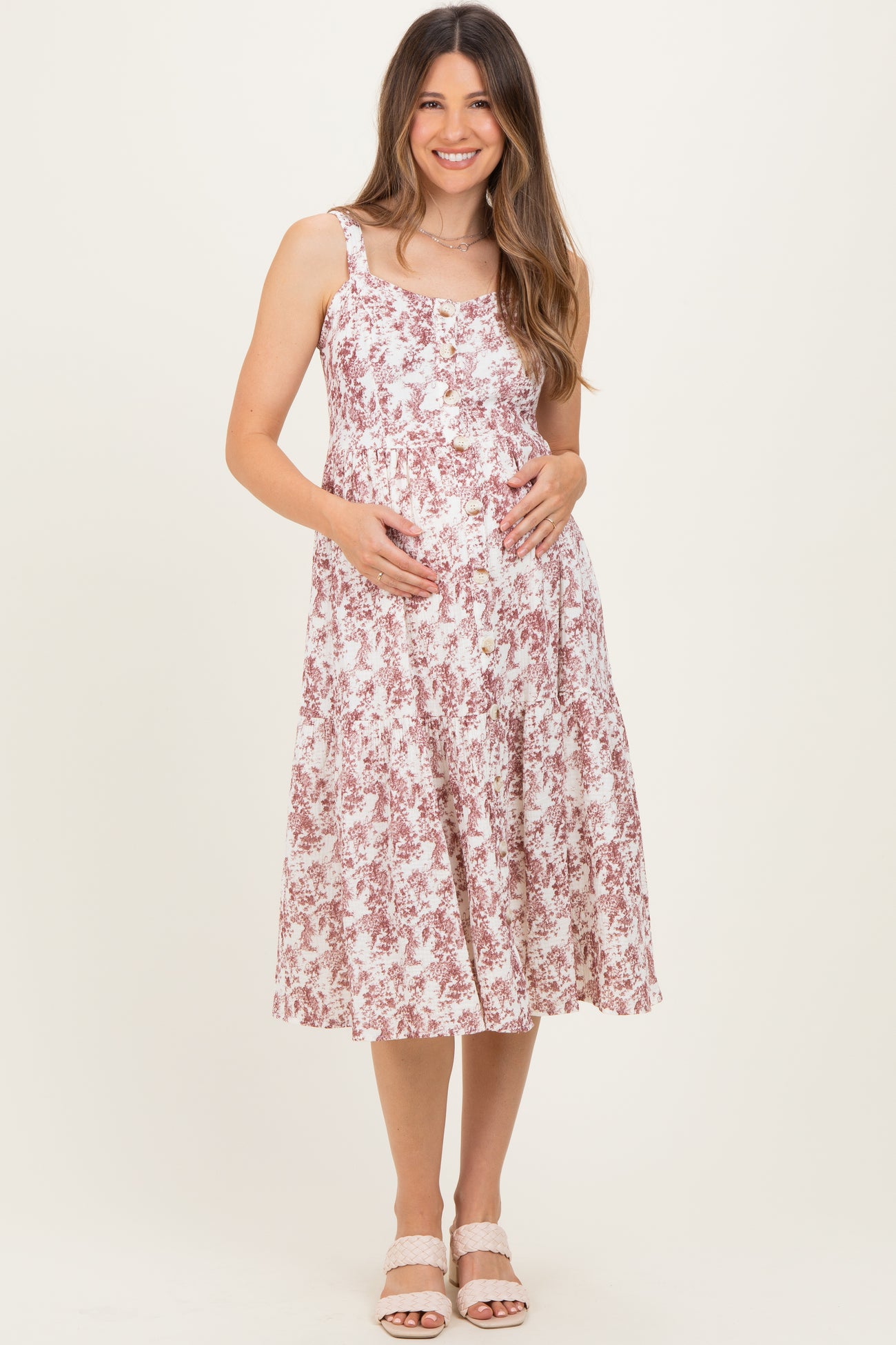 woman wearing a floral pink and white maternity dress with straps, showcasing her baby bump