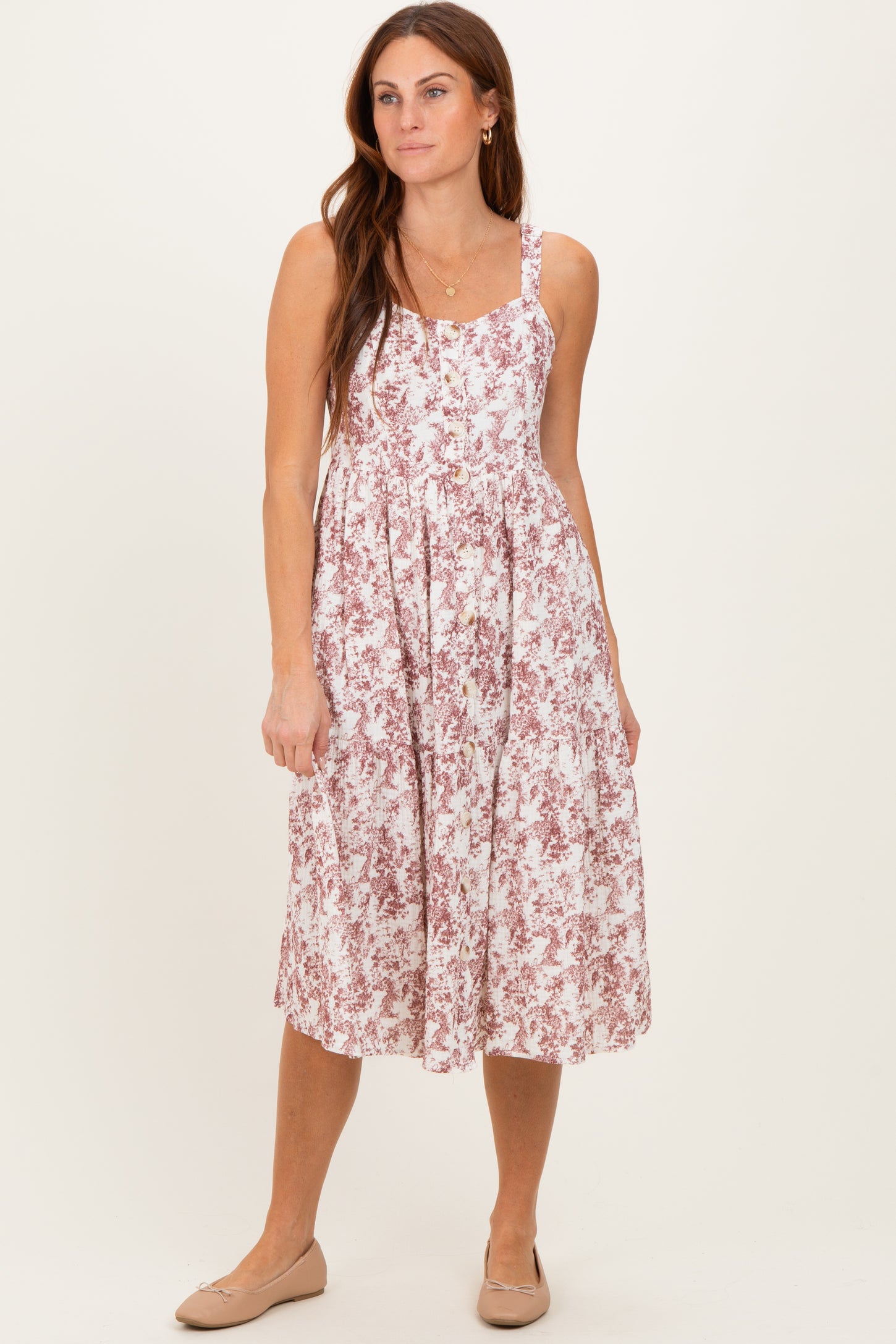 woman wearing a floral midi dress with spaghetti straps and a gathered skirt, standing and smiling