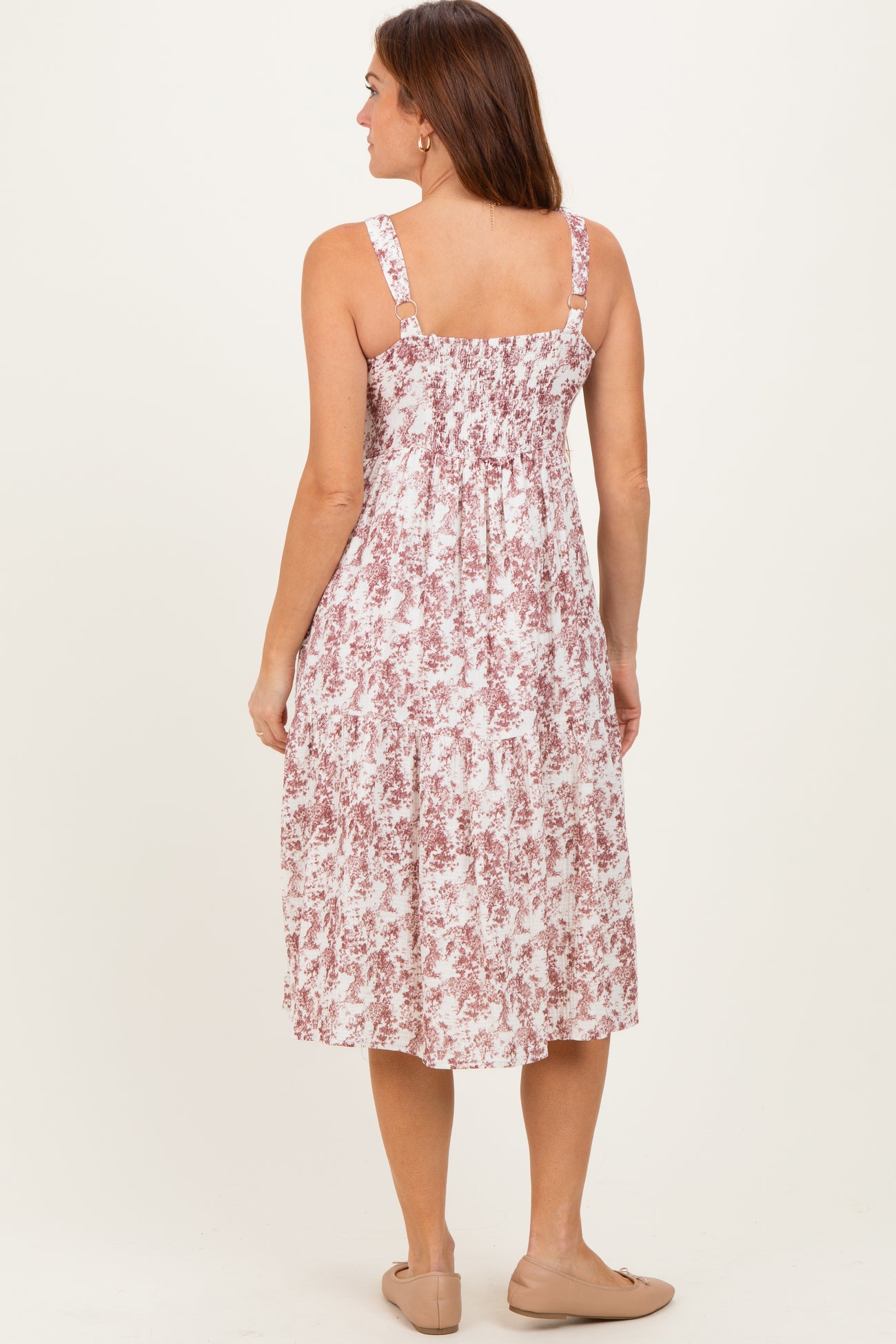 woman wearing a back view of a pink and white floral midi dress with adjustable straps and smocked bodice