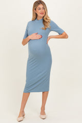 woman wearing a light blue short sleeve maternity dress and holding her baby bump