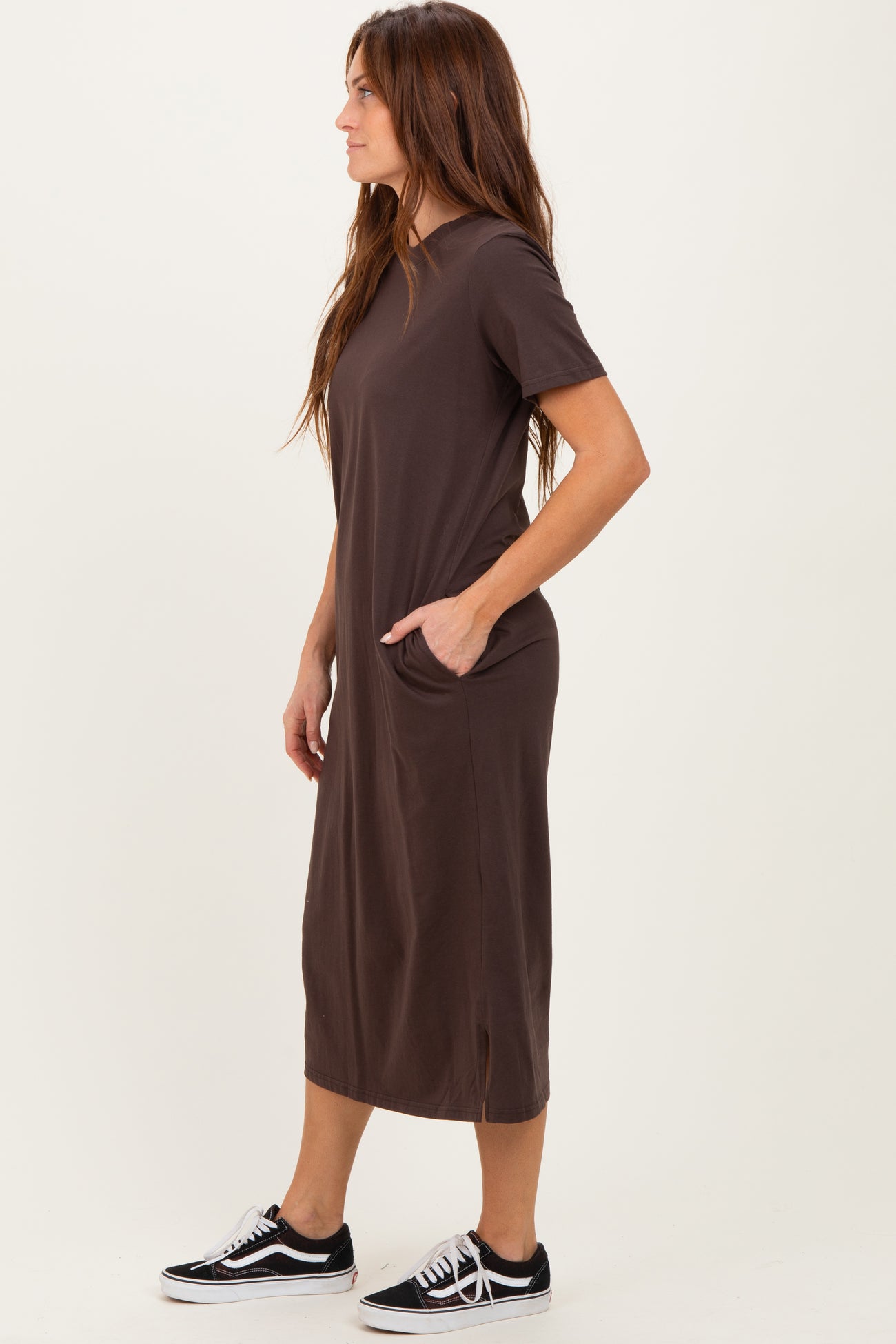 woman wearing a dark brown short sleeve maxi dress with side pockets and styled with black sneakers
