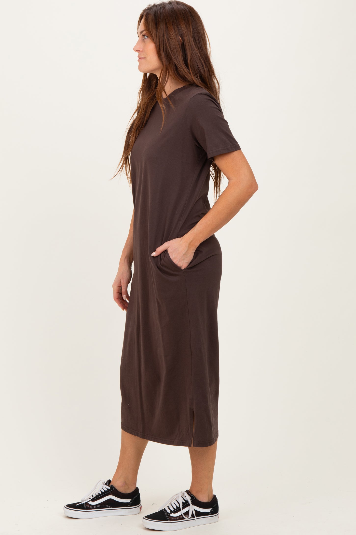 woman wearing a dark brown short sleeve maxi dress with side pockets and styled with black sneakers