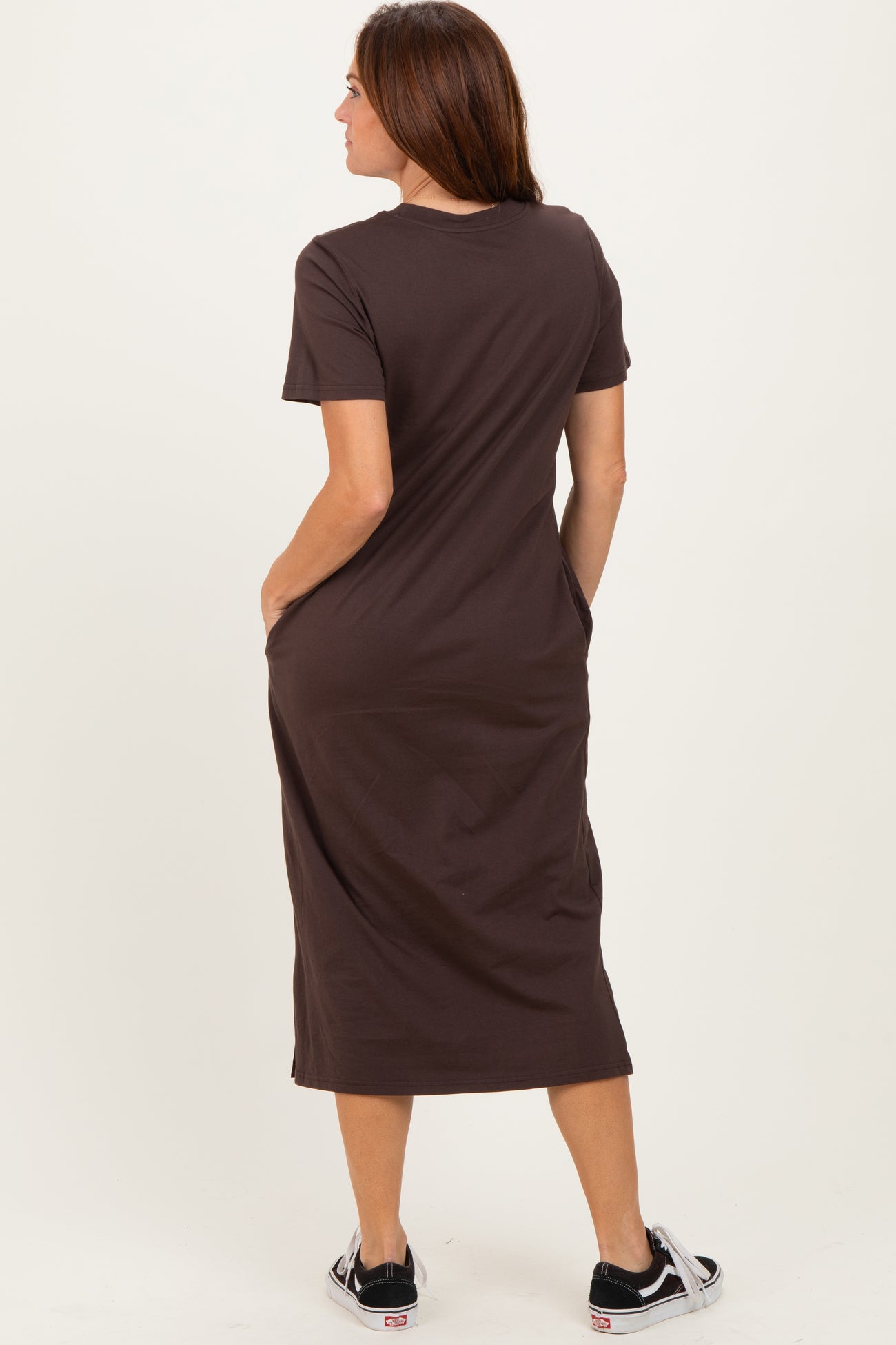 woman wearing a brown short sleeve maxi dress with pockets, standing with her back to the camera