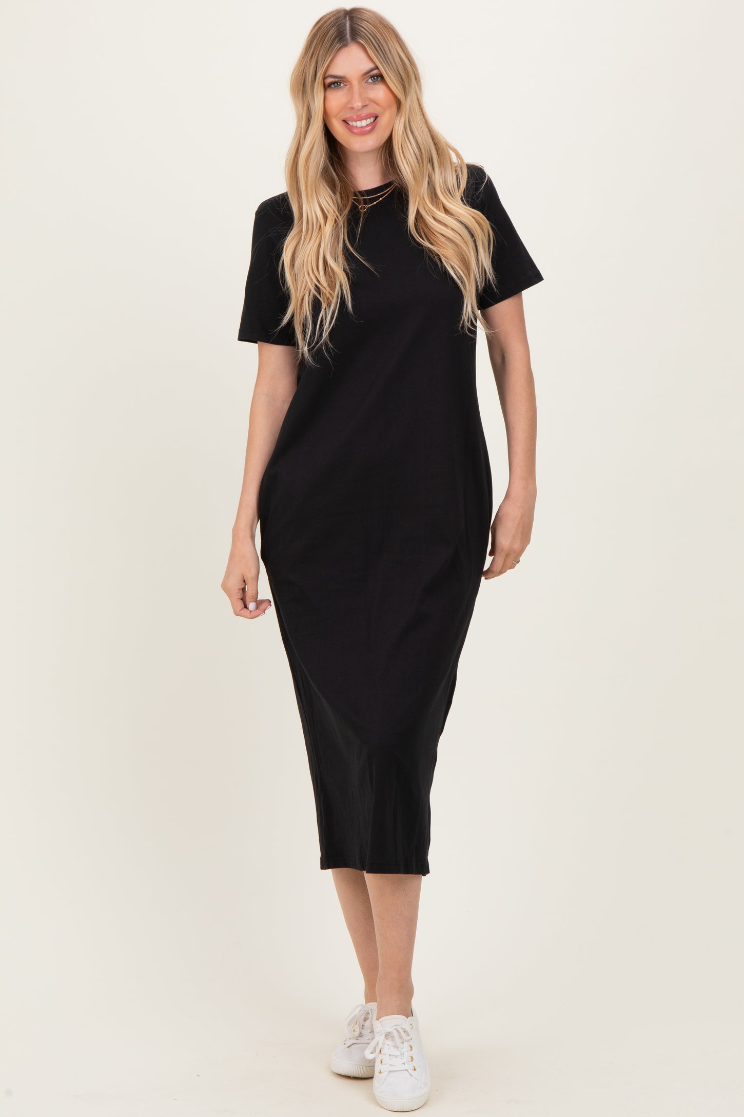 woman wearing a black short sleeve midi dress with a relaxed fit and side slits, paired with white sneakers