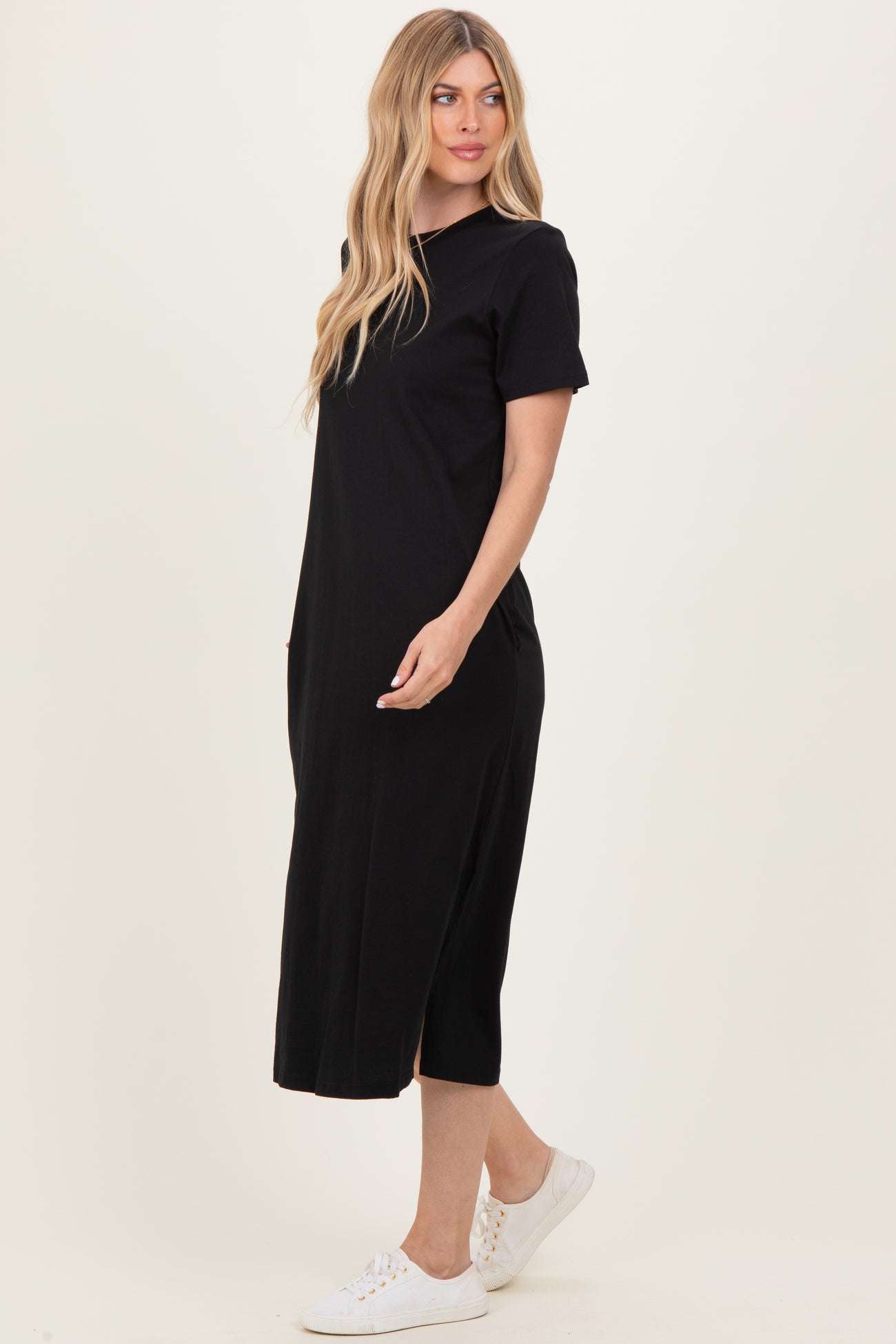 woman wearing a black midi t-shirt dress with side pockets and short sleeves, styled with white sneakers