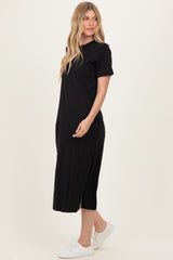 woman wearing a black midi t-shirt dress with side pockets and short sleeves, styled with white sneakers