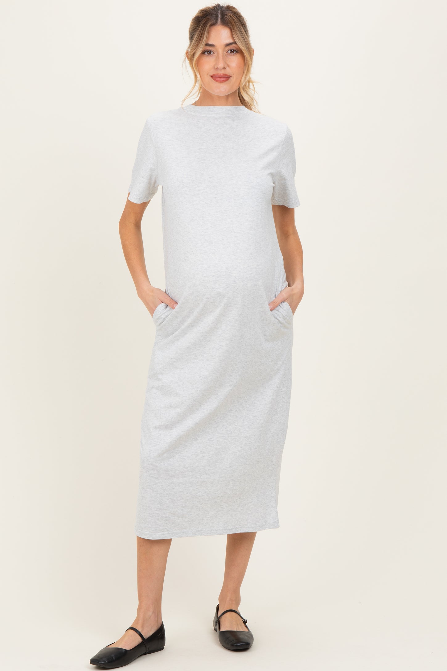 woman wearing a light grey short sleeve maternity dress with pockets and a baby bump visible